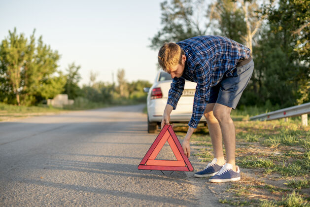 汽车一个年轻人拿着一个红色三角形 把它放在路上 标志着车祸服务安全修理