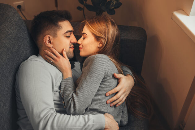 床早晨 一对迷人的年轻夫妇面带微笑地倚在沙发上 然后在家里的窗户边亲吻拥抱浪漫拥抱成人