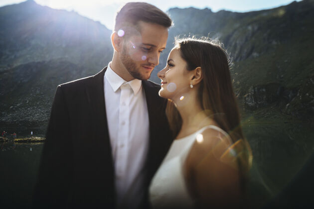 新郎侧视图一个惊人的新郎和新娘看着对方微笑着拥抱日出在山上的肖像山关系优雅