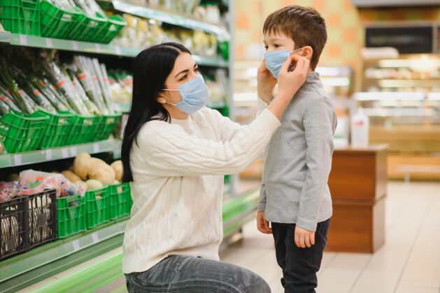 父母在冠状病毒流行或流感爆发期间 一名年轻女子和戴着防护面罩的孩子在超市选购食品女孩购物推车