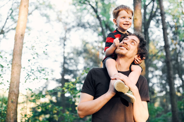 宝贝年轻的父亲在夏天和他的小儿子在公园里散步 把它扛在肩上父亲休闲玩