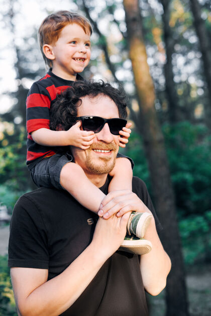 友谊年轻的父亲在夏天和他的小儿子在公园里散步 把它扛在肩上海洋天空手
