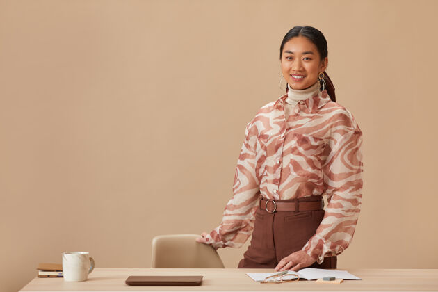 小企业亚洲年轻女商人站在米色墙壁旁 微笑着站在工作场所的前面工作自信上班族