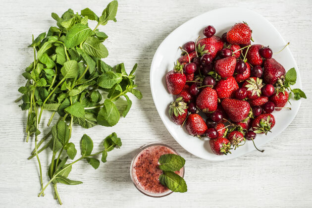 绿色白色木桌上放着草莓和樱桃 薄荷 水果冰沙的盘子俯视图顶视图浆果特写