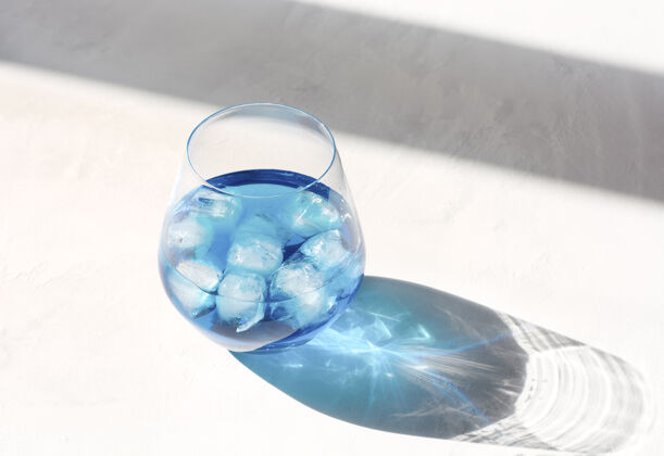 透明玻璃阳光明媚的日子里 蓝色蝴蝶豌豆冰汁装在一个透明的大玻璃杯里 放在一张灰色的桌子上清爽饮料冰茶热天