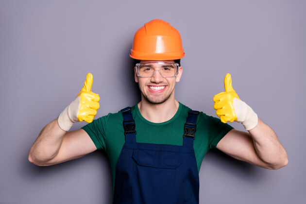 技师自信酷的维修工肖像有橙色安全帽黄色手套展示拇指向上标志批准重建公寓房间穿绿色t恤橙色隔离灰色墙壁手势修理工安全