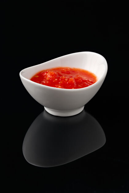 液体把酱汁放在一个白色的碗里 在黑色的表面上反射美食健康营养