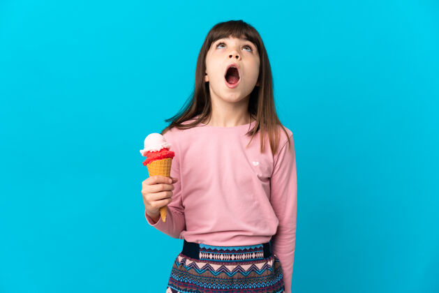 甜点一个拿着短号冰淇淋的小女孩站在蓝色的背景上 抬起头来 脸上露出惊讶的表情冰淇淋思想青春
