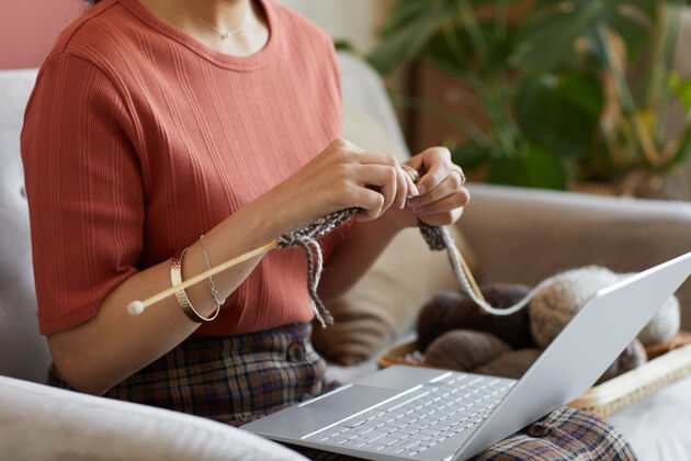 坐着坐在沙发上 膝上放着笔记本电脑 在家里织羊毛衫的女人的特写镜头仅成人成人无线技术