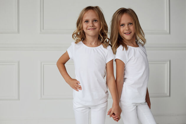 可爱正面是一对穿着白色衣服的双胞胎姐妹手牵手的画像年轻姿势快乐