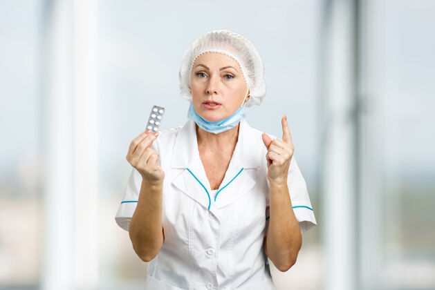 制服女医生拿着药丸中年女医生穿着白色制服吃药 用食指指着目录西装医院