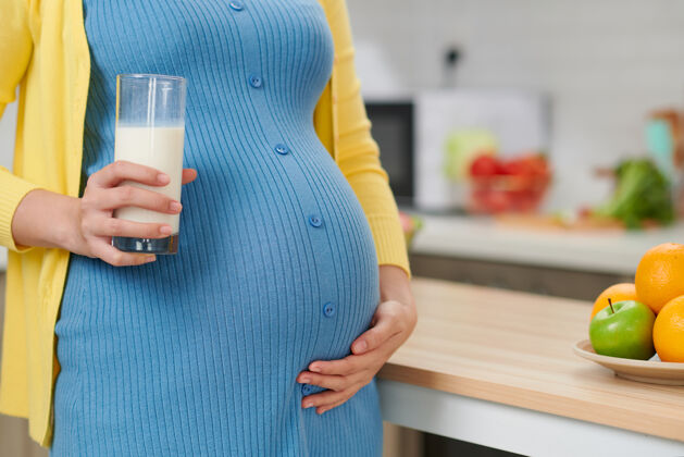 女人拿着一杯牛奶的年轻孕妇站在厨房里母亲生活人
