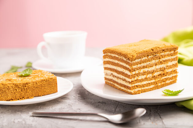 甜点自制蜂蜜蛋糕 牛奶奶油和薄荷 咖啡杯 粉色表面和绿色纺织品卡路里零食曲奇