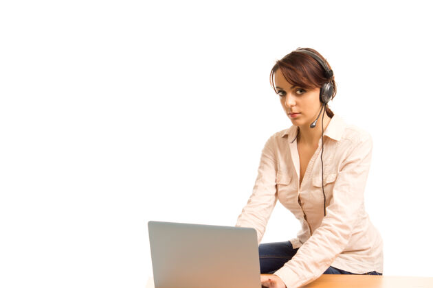 工人年轻迷人的私人助理或接待员 戴着耳机 坐在桌旁的笔记本电脑旁工作女士笔记本电脑服务