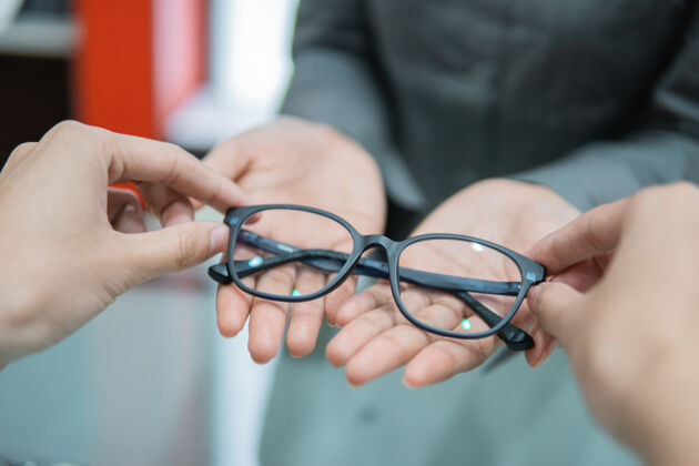 持有在一家眼镜店 售货员的手把一副眼镜递给顾客的手诊所眼镜商零售
