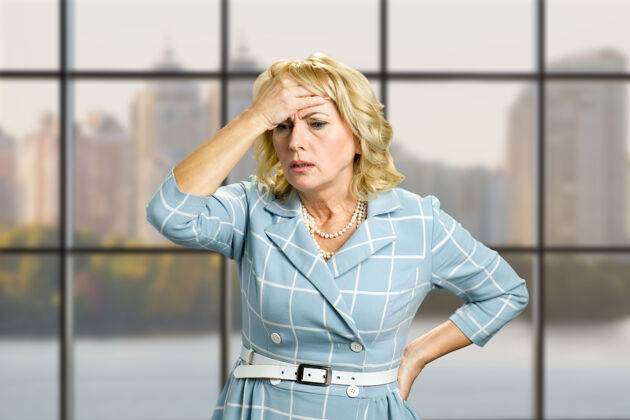 老年人办公室里忧心忡忡的女人办公室窗户上有头痛 偏头痛或健忘的压力很大的女商人头痛手担心