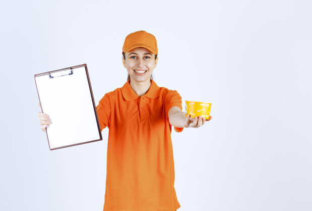 促销身着橙色制服的女快递员拿着一个黄色的面杯 要求签名员工送货越南