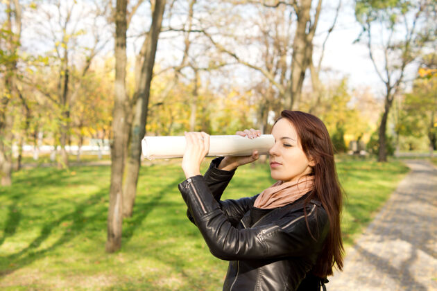 女人一个女人站在公园的户外 用一张卷起的报纸对着她的眼睛窥视远处人年轻年轻