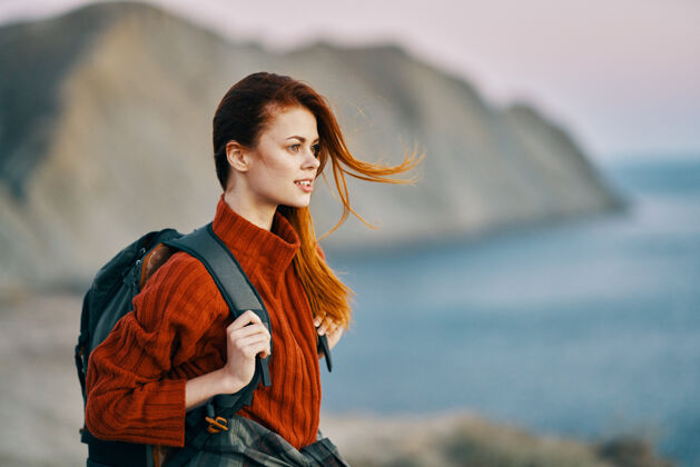 洞穴红发旅行者背着一个背包 穿着一件毛衣 在海滩附近的山区天气海岸悬崖