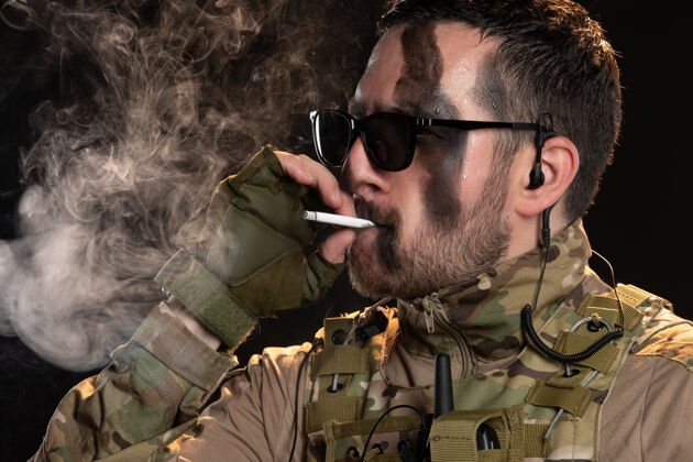 人穿迷彩服的男战士在黑墙上抽烟香烟衣服肖像
