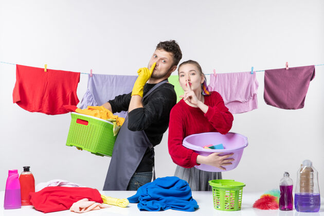 快乐的年轻夫妇幸福的年轻夫妇正对着白色墙上拿着洗衣物的安静标志人制造洗