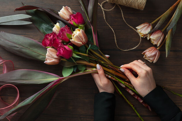 花店工作中的花店：婦女在木制背景上用不同的鮮花制作時尚的現代花束級在婚禮 母親節 婦女節送給新娘的禮物浪漫的春季時尚激情玫瑰作品園藝女孩