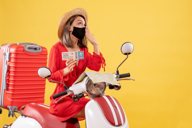 肖像正面图：戴着黑色面罩的年轻女士 骑着轻便摩托车 提着红色手提箱 打着哈欠旅行红色持有