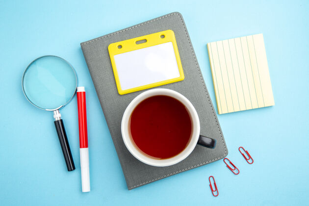 红茶一杯红茶的顶视图在灰色笔记本上放大镜笔在蓝色表面玻璃粉末陀螺