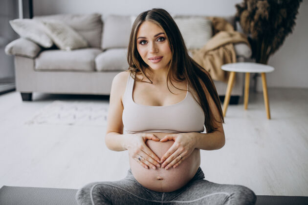 腹部孕妇在家里的垫子上练习瑜伽期望运动分娩