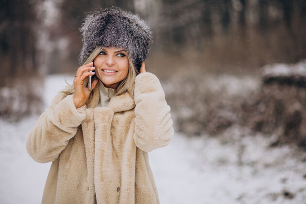移动穿着冬衣的女人走在满是雪的公园里打电话自然树女孩