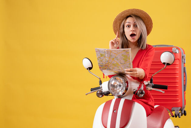 肖像骑着轻便摩托车的漂亮女孩拿着红色的手提箱 拿着一张令人惊讶的地图惊喜坐着时尚