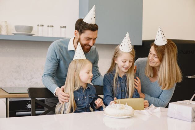 脚踝一家人和他们的两个女儿在厨房庆祝生日人们戴着派对帽女孩用盒子装礼物厨房盒子服装