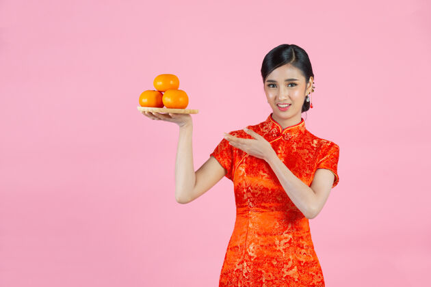 文化美丽的亚洲女人开心地微笑着 手里拿着粉红背景的新鲜橘子过年展示衣服微笑