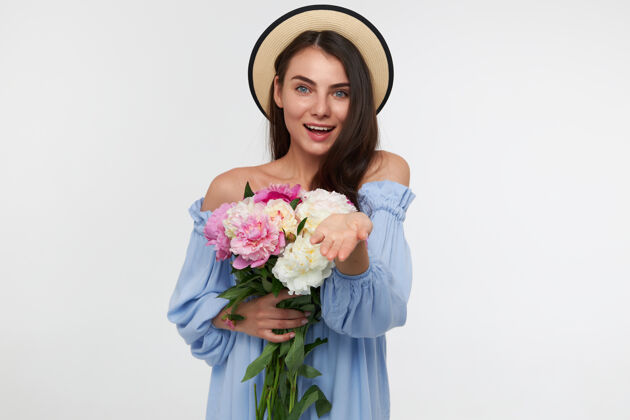 年轻一个快乐的女人 深色长发 戴着帽子 穿着蓝色的裙子 手里拿着一束花 手掌张开长发花束肖像