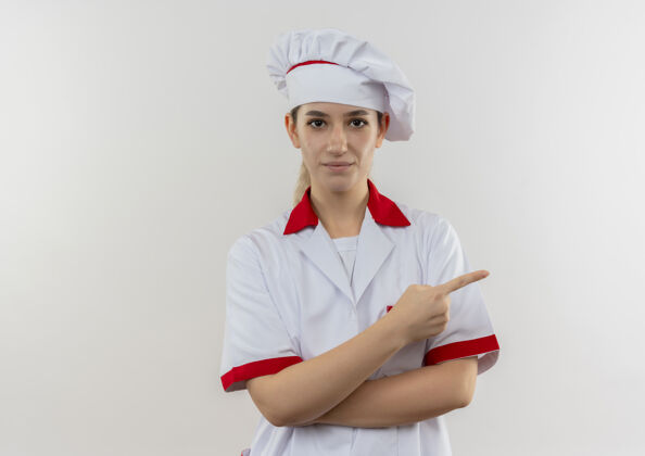 指点自信的年轻漂亮厨师 身着厨师制服 指着隔离在白色墙壁上的一侧 留有复印空间年轻制服漂亮