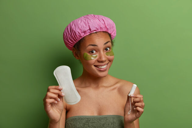 定期健康微笑的女模特裹着浴巾 戴着绿色的眼罩选择胶原蛋白毛巾