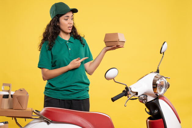 送货正面图身着绿色制服的女快递员 黄色背景上有一个小食品包 工作颜色为工作递送食品服务人员食物包装服务