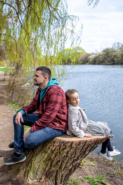 公园早春时节 爸爸和他的小女儿坐在河边的森林里 享受大自然爱父亲关心