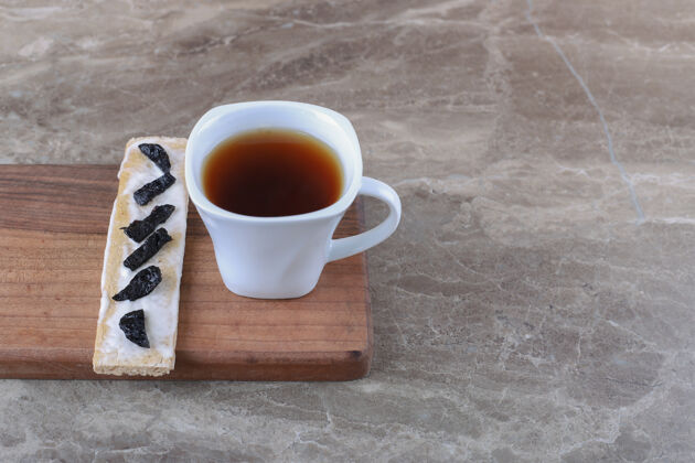 年糕把干李子片放在酥皮面包上 把一杯茶放在木板上 放在大理石表面面筋大米茶