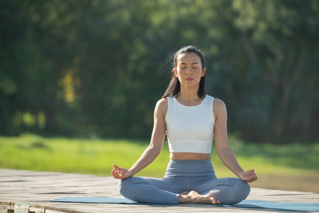 人坐在瑜伽垫上的女士在山湖公园放松安静的女士闭着眼睛练习瑜伽 坐在垫子上的帕德马萨纳姿势 莲花练习 穿着运动服的迷人运动女孩运动女性早晨