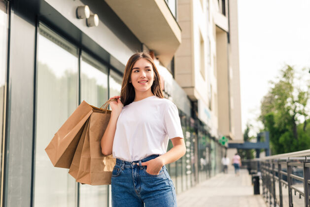 模型带着购物袋走在城市街道上的年轻漂亮女人手购买购买