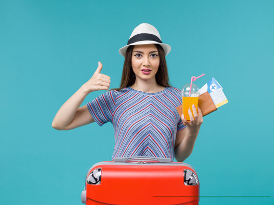美丽前景度假的女人拿着她的红包拿着机票和果汁在蓝色背景上旅行度假的女人包举行肖像