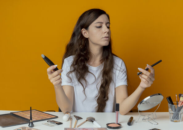 坐着年轻漂亮的女孩坐在化妆台上拿着化妆工具 看着睫毛膏和睫毛膏睫毛膏拿着眼线笔