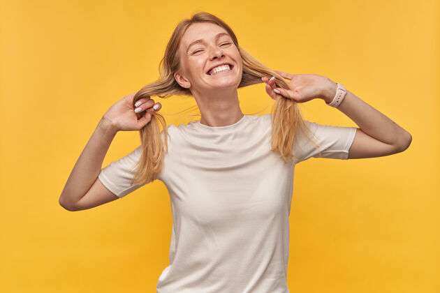 衣服快乐俏皮的女人 长着雀斑 穿着白色T恤 扎着马尾辫似的头发 黄色的脸上带着微笑自信金发抱着