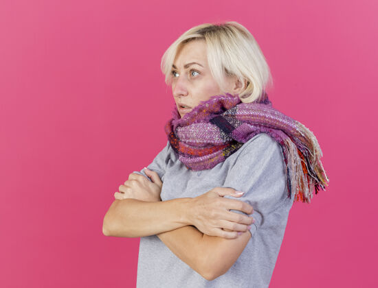 疾病冻僵的年轻金发病斯拉夫妇女戴着围巾抱着手臂看着粉红色的一面女人胳膊围巾