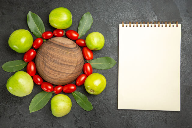 葡萄顶视图樱桃西红柿绿色西红柿和月桂叶围绕一个木制盘子和一个笔记本在黑暗的地面上食物苹果水果