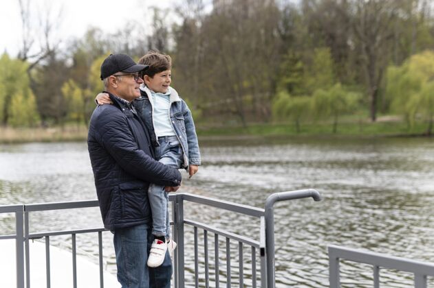 人老人抱着孙子在湖边的公园里外部男孩祖父