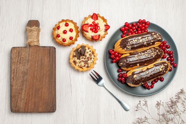餐厅俯视图：灰色盘子上的巧克力蛋糕和葡萄干饼干白色木桌上的叉子和砧板午餐胡椒排骨
