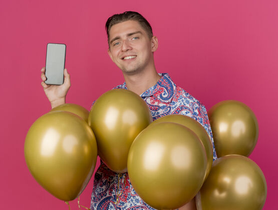 穿着面带微笑的年轻人穿着五颜六色的衬衫站在气球中间 手里拿着粉红色的手机等等抱着气球