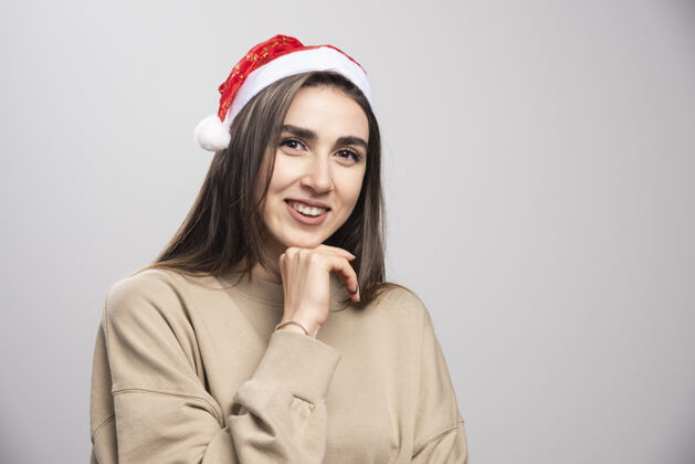 抱着戴着圣诞老人帽子的年轻女子在摄影棚拍摄了一张灰色的照片年轻女性圣诞老人